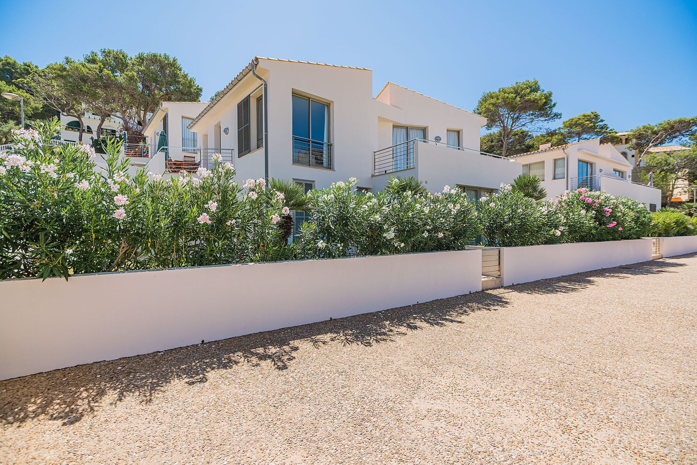 A modern two-story building with a white exterior, a balcony, and a gravel driveway.