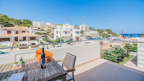 Een balkon met een tafel, stoelen en een fles wijn, met uitzicht op een kustplaatsje met gebouwen en een heldere lucht.