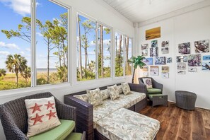 Ein Zimmer mit großem Fenster und Blick auf eine natürliche Landschaft, mit Korbmöbeln und Wandbildern.