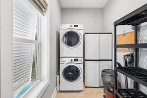 A laundry room with stacked washers and dryers, a window with blinds, and a shelf with cleaning supplies. - Bay Front w/ Private Saltwater Pool and Dock (Port St. Joe)