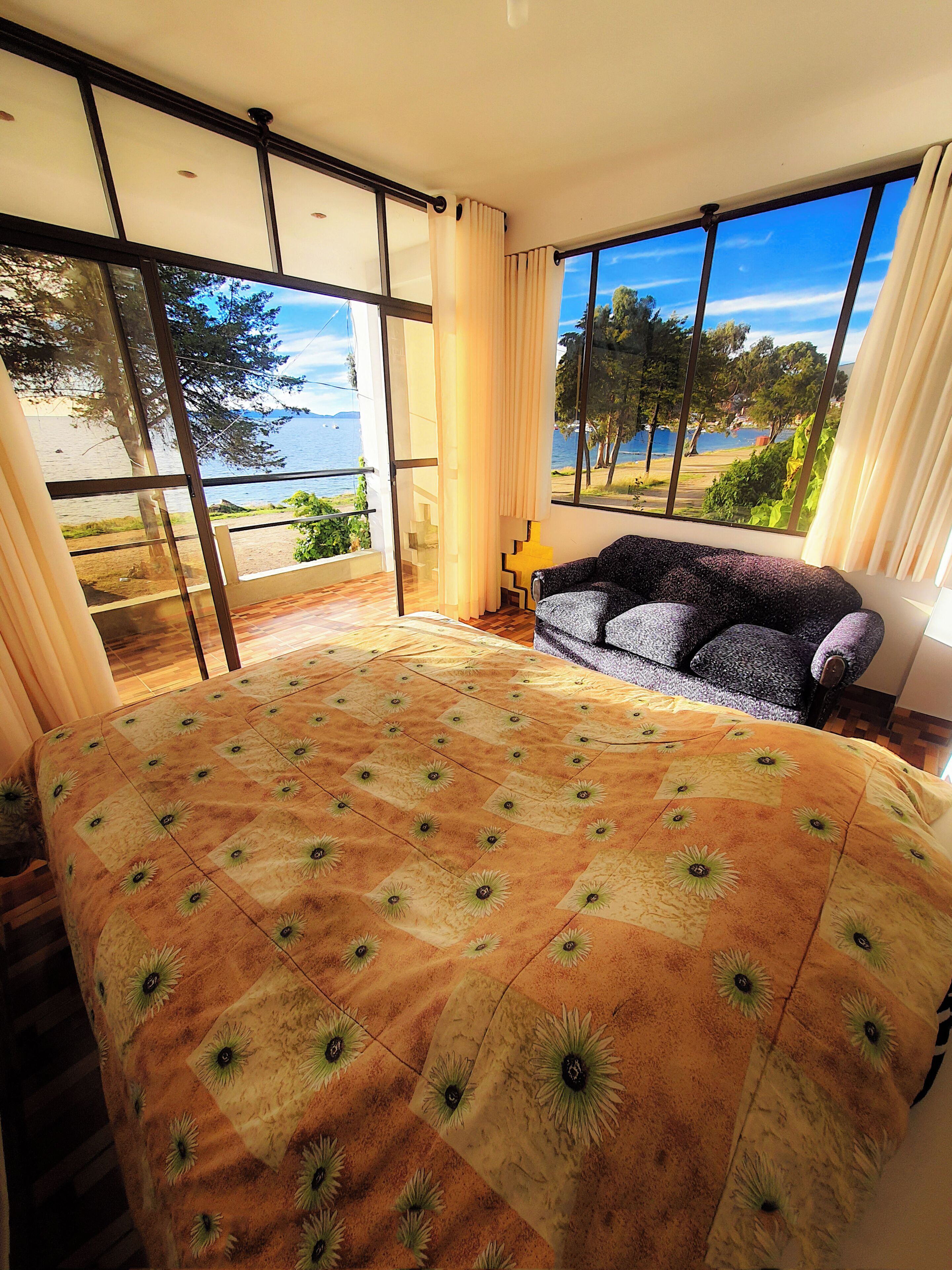 A bedroom with a large bed, a sofa, and a view of a lake through large windows.