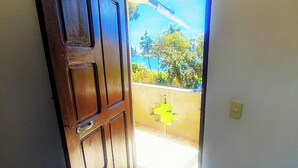An open wooden door leading to a balcony with a tiled floor and a view of a coastal landscape.
