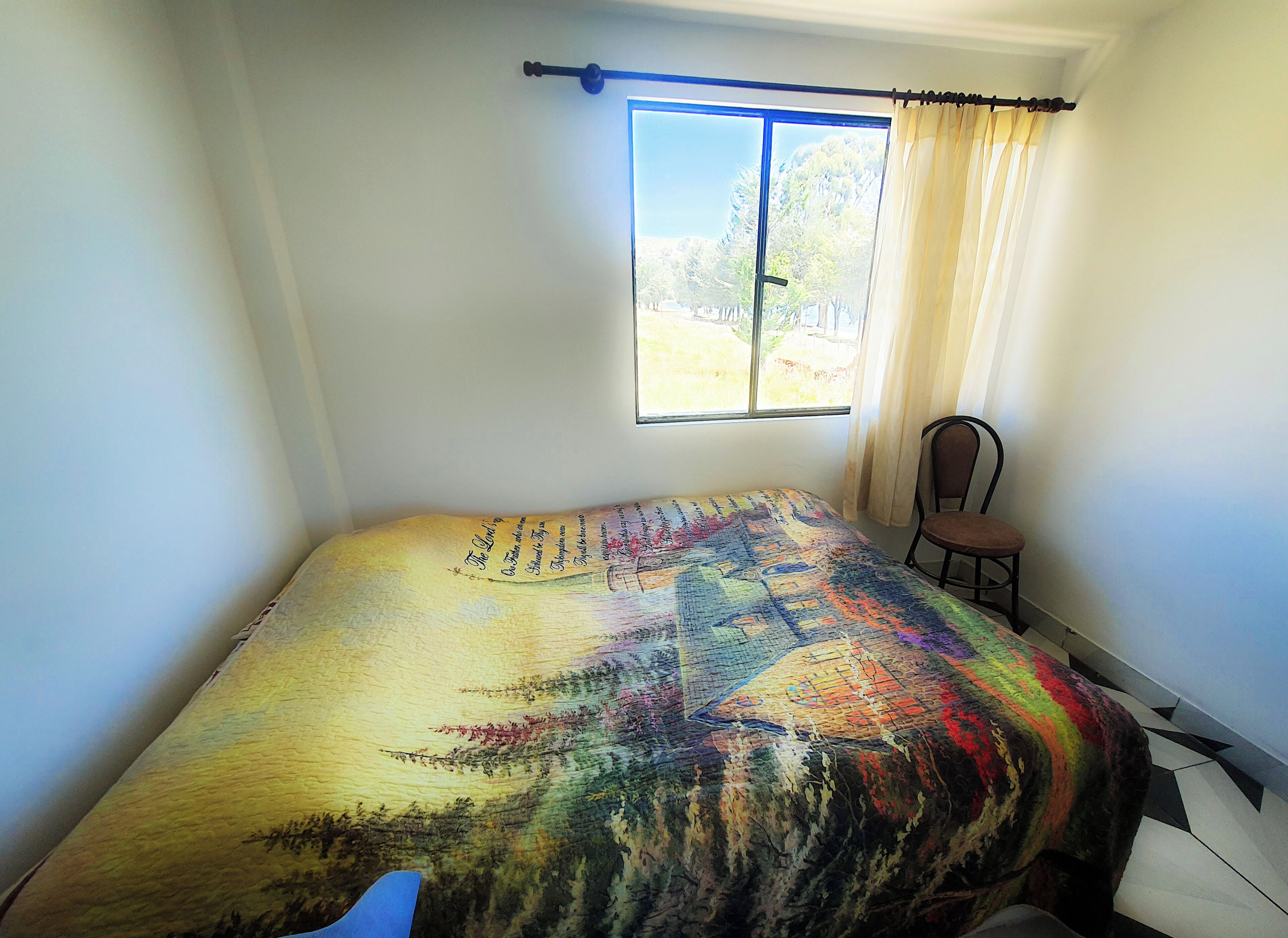 Un dormitorio con cama, una silla, una ventana con cortinas y vistas al exterior.
