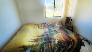Un dormitorio con cama, una silla, una ventana con cortinas y vistas al exterior.