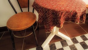 Un comedor con una mesa cubierta con un mantel estampado, una silla con asiento acolchado y un jarrón con flores rojas.