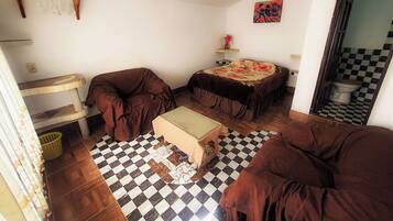 A small, compact room with a checkered floor, a bed with a floral bedspread, a sofa, a small table, and a cat tree.