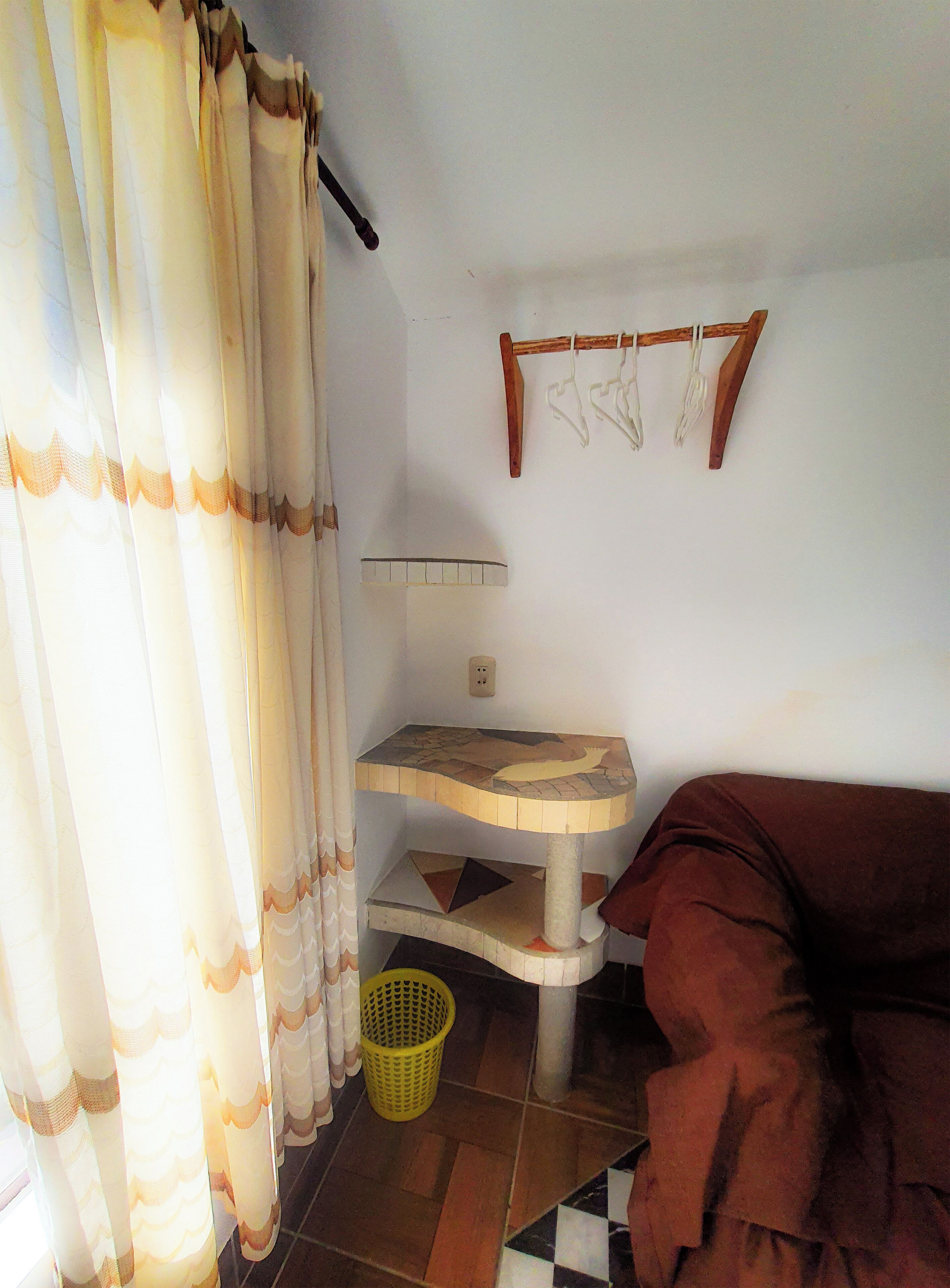 A room with a cat tree, a sofa, a curtain, a wall-mounted rack, and a tiled floor.