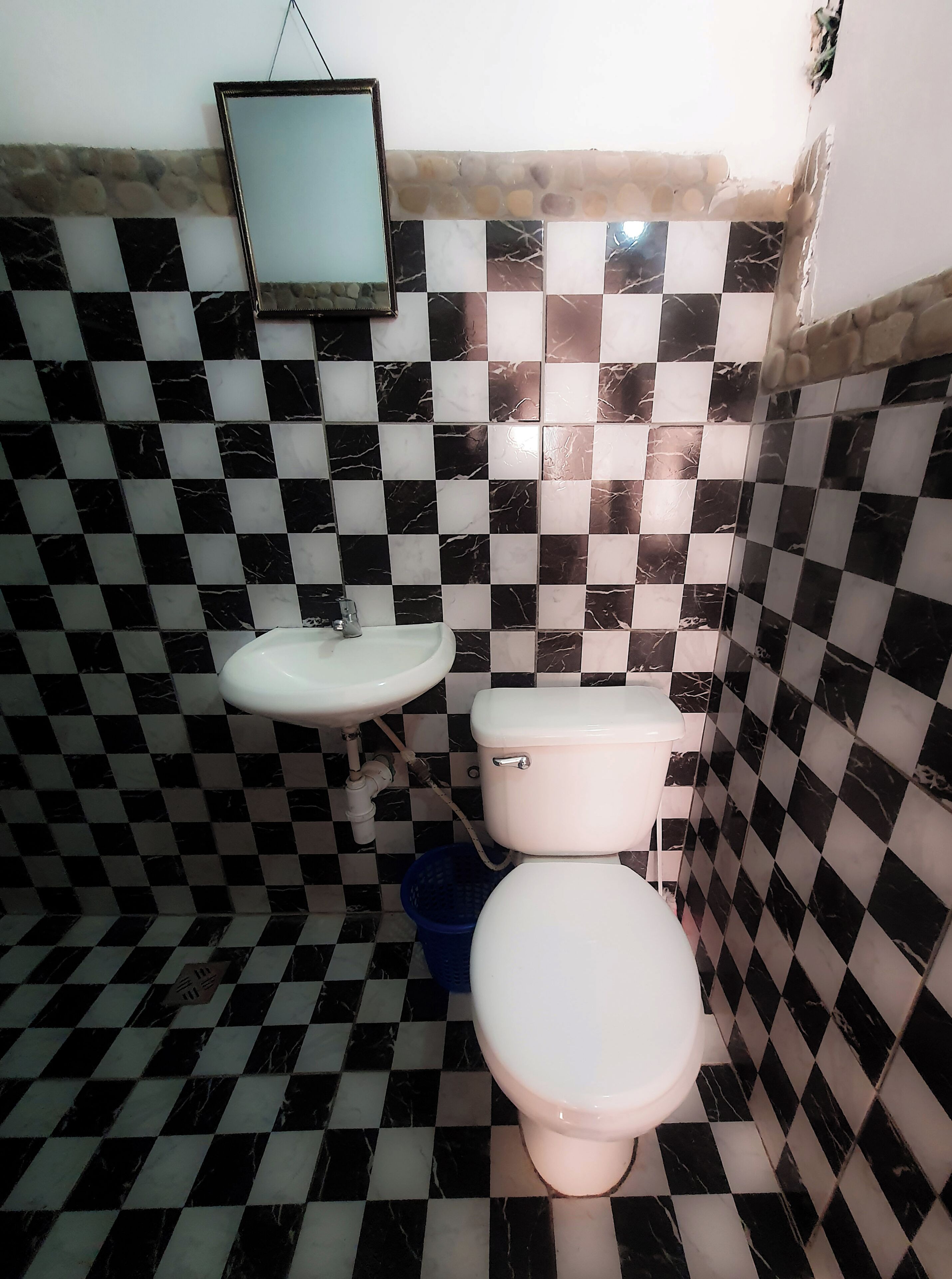 A bathroom with a checkered floor pattern, a sink, a toilet, and a mirror.