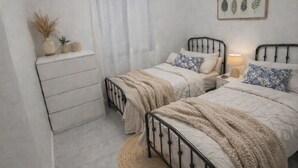 A bedroom with two beds, a bedside table, a round rug, and a ceiling light.