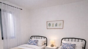 A bedroom with two single beds, a bedside table with a lamp, a round rug, and a ceiling light. - Modern villa with a large private above-ground pool – 3 bedrooms (Vacqueyras)