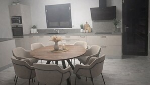 A modern kitchen with a dining area, featuring a round wooden table and six chairs, a built-in oven, and a large window above the sink. - Modern villa with a large private above-ground pool – 3 bedrooms (Vacqueyras)