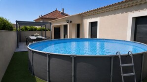 A round above-ground pool with a ladder, surrounded by artificial grass, and a patio area with a table and chairs. - Modern villa with a large private above-ground pool – 3 bedrooms (Vacqueyras)