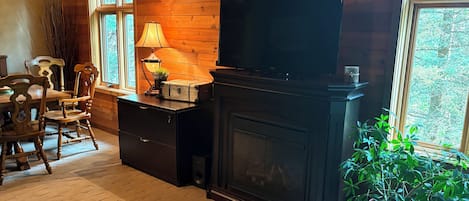Una habitación acogedora con chimenea, paredes de madera, televisor, escritorio con lámpara y planta en maceta.