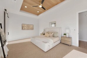 Ein Schlafzimmer mit einem Bett, Nachttischen, einem Deckenventilator, einem an der Wand befestigten Spiegel und einem gerahmten Bild.
