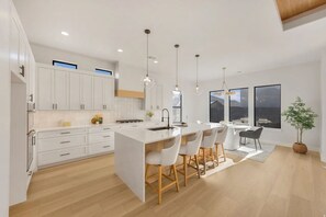 A modern kitchen with white cabinetry, a central island with bar stools, and pendant lighting. - Fully Furnished Modern Desert Retreat in Hurricane (Hurricane)