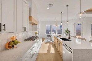 Une cuisine moderne avec des meubles blancs, un îlot central, des luminaires suspendus et une vue sur l’extérieur.