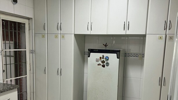 Una cocina con armarios blancos, compartimentos de almacenamiento numerados y un refrigerador con imanes.
