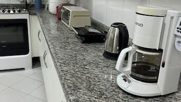 Une cuisine équipée d’une cuisinière à gaz, d’un grille-pain, d’une bouilloire et d’une machine à café, le tout posé sur un plan de travail en granit.