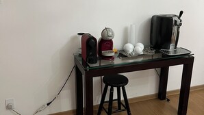Una pequeña mesa de madera oscura con un tablero de vidrio, un taburete negro y una cafetera.