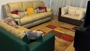 Una sala de estar con un sofá, un sillón verde, un sofá de mimbre y un televisor.