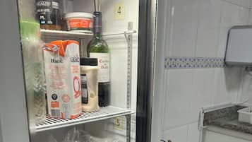 Uma cozinha com geladeira repleta de alimentos diversos, uma pia e bancada com micro-ondas.