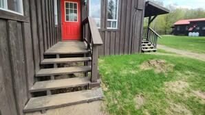 A wooden cabin with a red door, a staircase leading to a porch, and a sign indicating the entrance to a campground. - Cozy stay at Haliburton Forest. Trails, Wolf Centre, Canopy Tour, 100 lakes! (Dysart and Others)