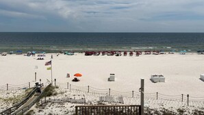 Ein Strand mit einer Holzpromenade, die zum Ufer führt, mit Sonnenschirmen und freiem Blick auf das Meer.