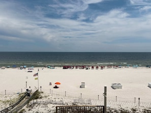 Ein Strand mit einer Holzpromenade, die zum Ufer führt, mit Sonnenschirmen und freiem Blick auf das Meer.