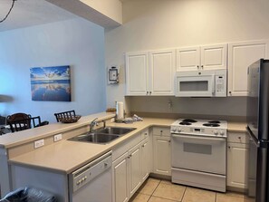 A kitchen with white cabinets, a stainless steel sink, a stove, and a microwave.