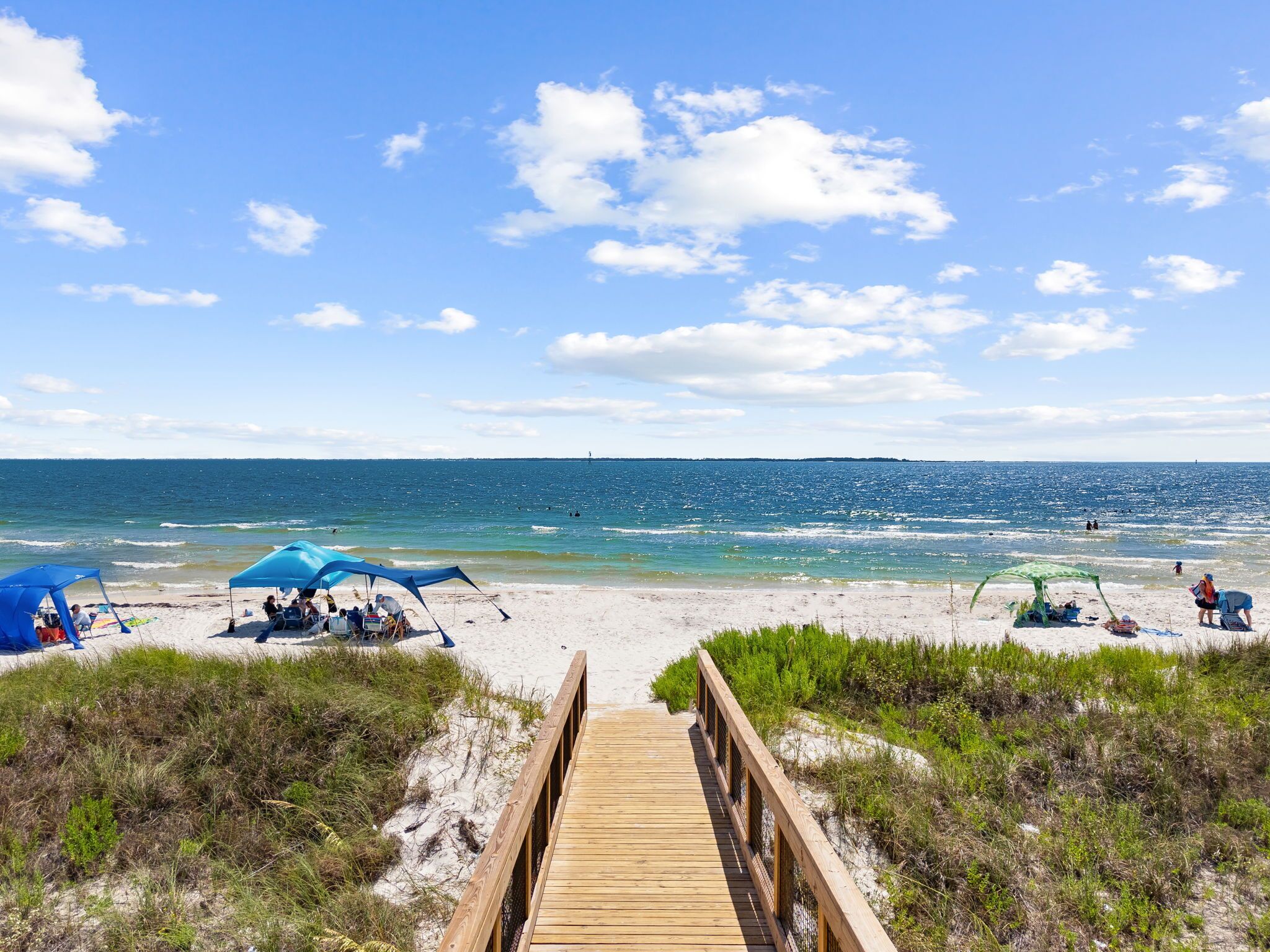 A wooden boardwalk leading to a beach with tents and people.