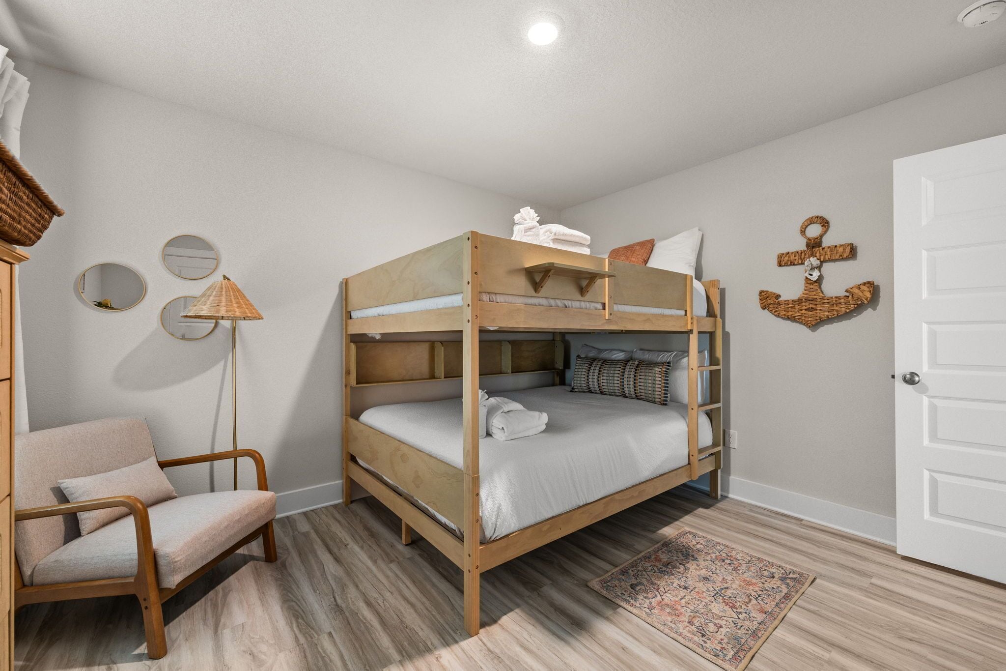 A bunk bed with a wooden frame, a chair with a cushion, a floor lamp, and a decorative wall anchor.