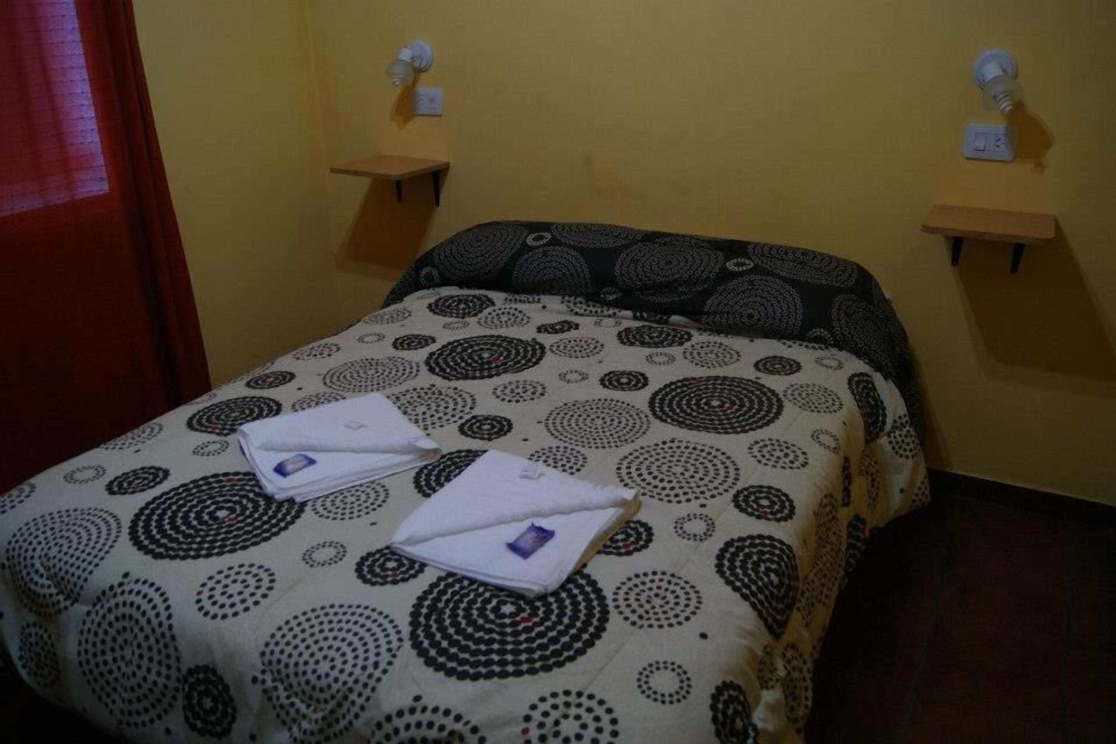 Une chambre d’hôtel avec un lit, deux tables de chevet et un luminaire fixé au mur.