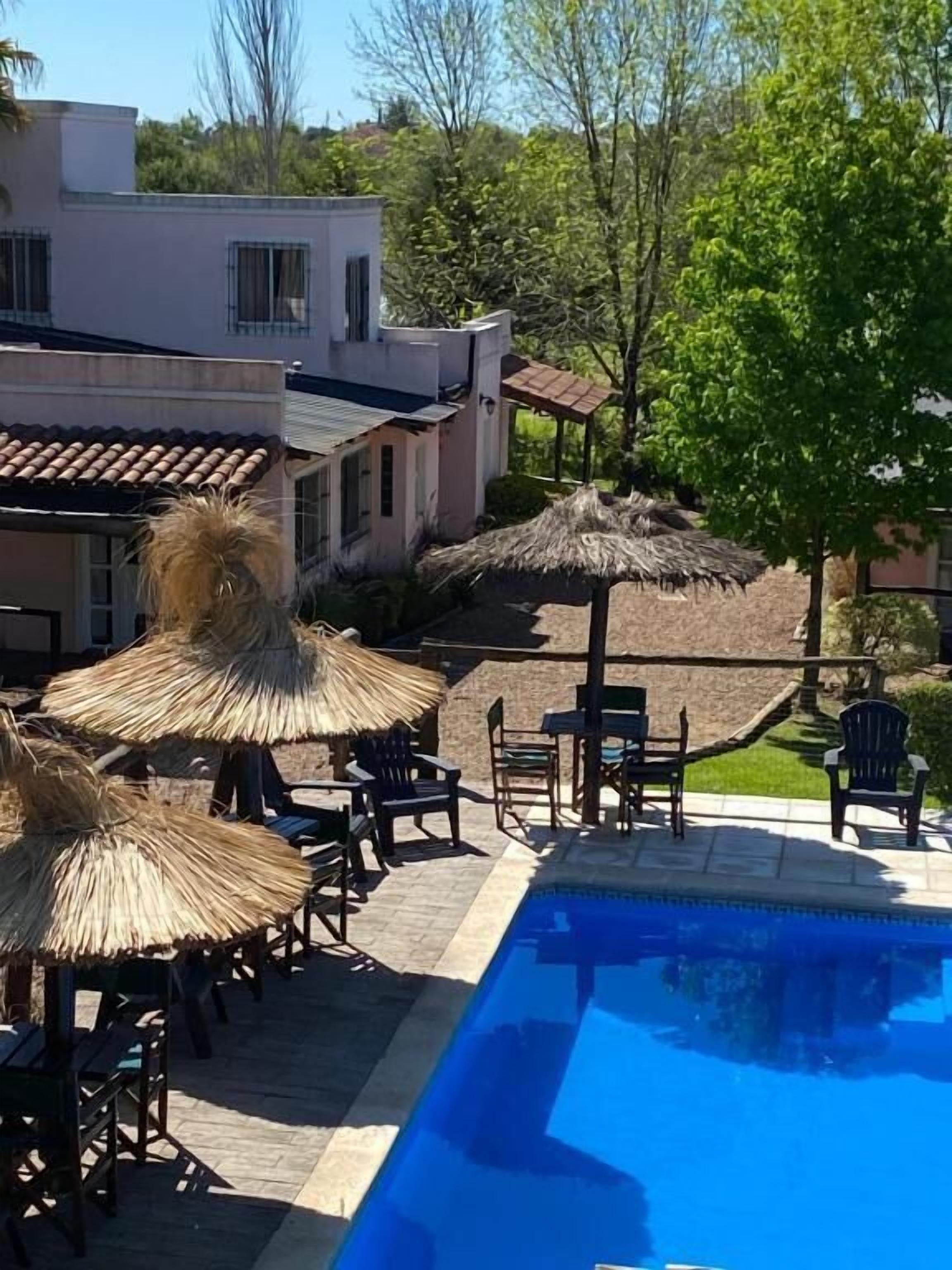 Zona de piscina con sillones de descanso y sombrillas, rodeada por un edificio con tejado de baldosas.