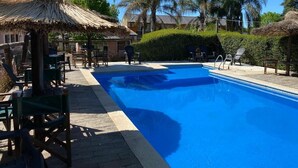 Una piscina con sillones de descanso y una estructura con techo de paja.