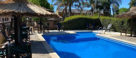 A swimming pool with lounge chairs and a thatched roof structure.
