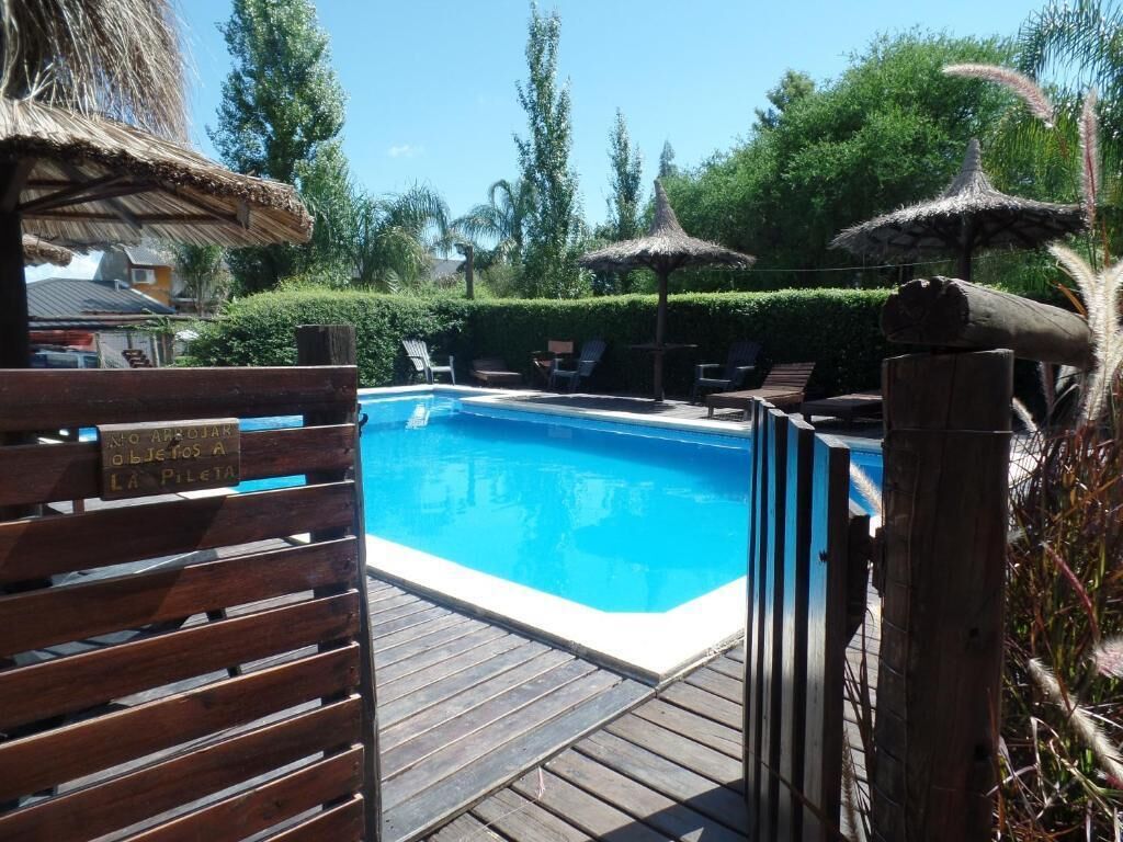 Zona de piscina con terraza de madera, sillas de descanso y sombrillas de paja.