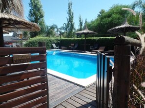 A swimming pool area with wooden deck, lounge chairs, and thatched umbrellas. - Cabañas Peumayen (Colón)