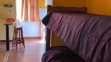 Una habitación con sofá, una mesita, una silla y una cortina.