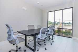 A conference room with a large table and four office chairs, large windows with a view of a parking lot and greenery, and a ceiling-mounted fire alarm. - Cozy 1-bedroom apartment in peaceful Houston with AC, pool, and gym access (Houston)