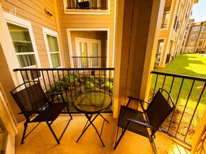 A balcony with two chairs and a table, overlooking a well-maintained lawn and neighboring buildings. - Cozy 1-bedroom apartment in peaceful Houston with AC, pool, and gym access (Houston)
