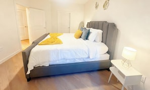 A bedroom with a bed, bedside table, lamp, and a door leading to another room. - Cozy 1-bedroom apartment in peaceful Houston with AC, pool, and gym access (Houston)