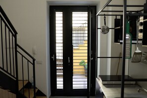 Eine Treppe führt zu einer Tür, von der aus man einen Balkon und eine Küchenzeile mit Herd und Geschirr sieht.