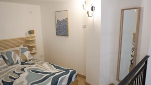 Et soveværelse med en seng, et natbord, en vægmonteret lampe, et indrammet billede og et spejl.