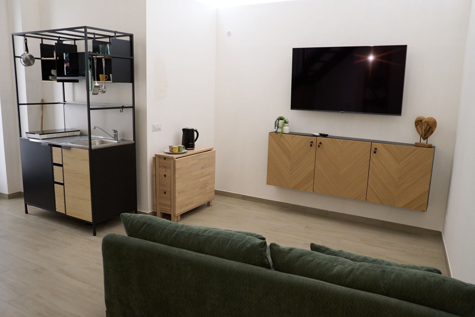 A modern living space with a kitchenette, a sofa, a TV, and a wooden cabinet.