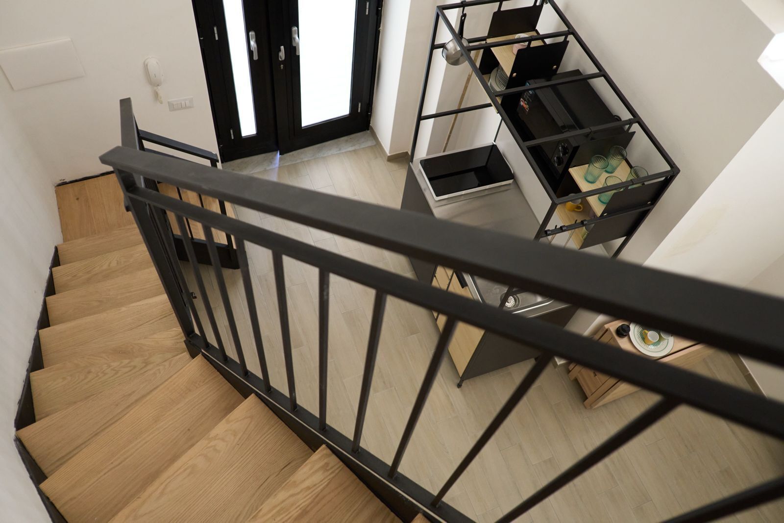 Eine Holztreppe mit schwarzer Metallreling, die zu einem Raum mit einem schwarzen Metallregal führt.