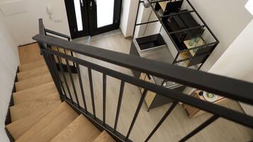 Eine Holztreppe mit schwarzer Metallreling, die zu einem Raum mit einem schwarzen Metallregal führt.