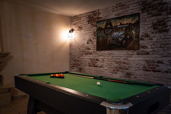 A pool table with balls, a wall clock, and a painting of a car.