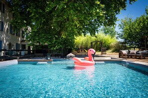 A swimming pool with a pink flamingo float, surrounded by trees and lounge chairs.