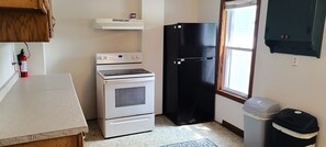 A compact kitchen with a stove, oven, refrigerator, and a trash bin. - Centrally located 3-bedroom house near beach, boardwalk, brewery, bars, and park (Algoma)