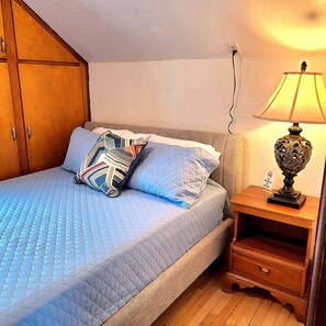 Ein Schlafzimmer mit Bett, Kissen, Nachttisch, Lampe und Kleiderschrank.